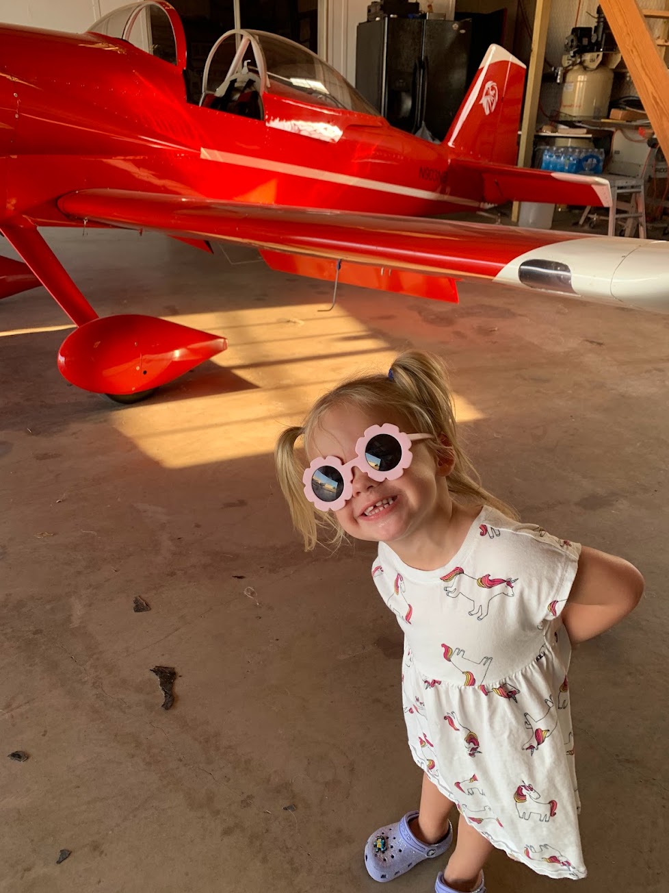 A child in sunglasses smiling in front of a red RV aircraft in the hangar